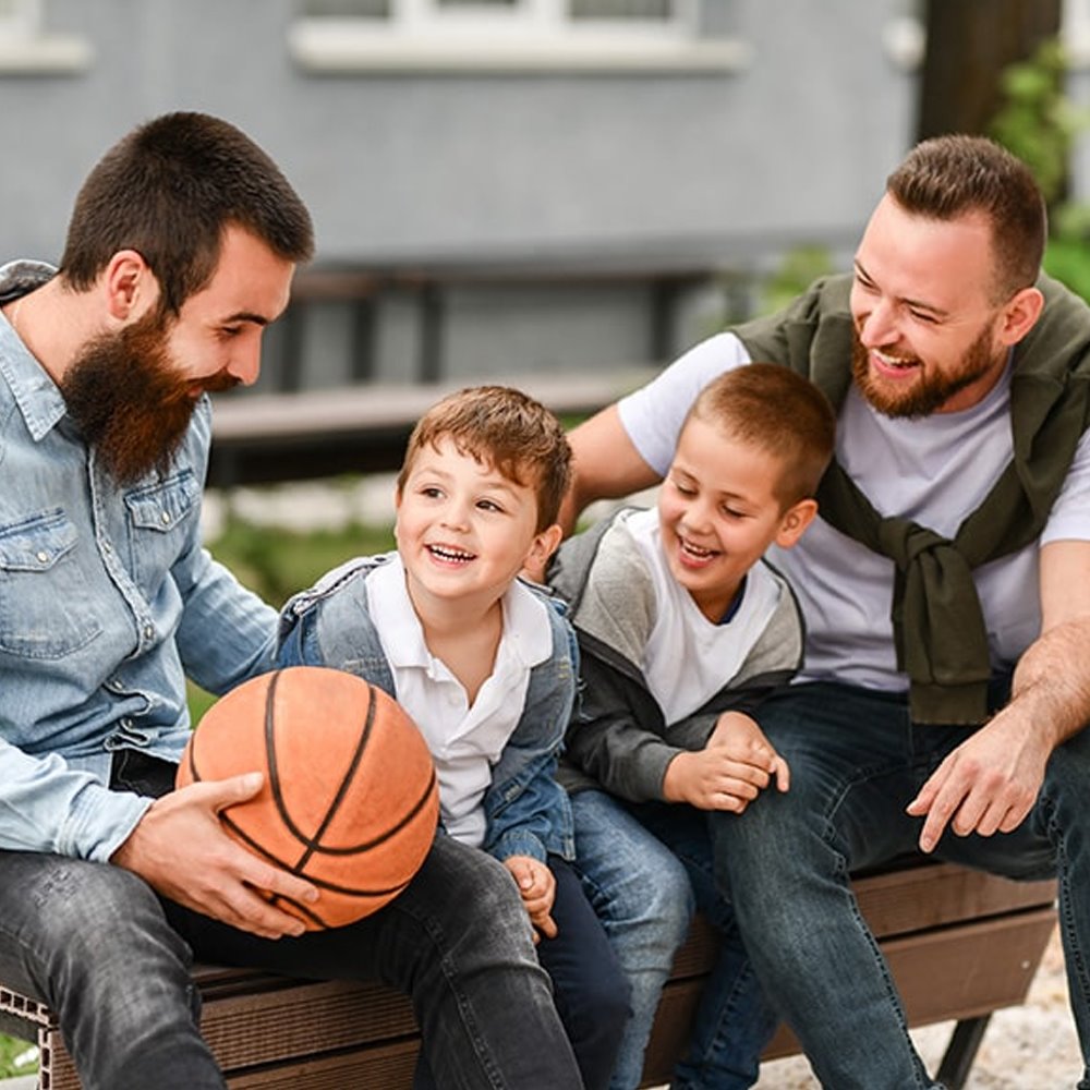 Two fathers and their children sitting on a bench with a basketball, representing an active and healthy lifestyle