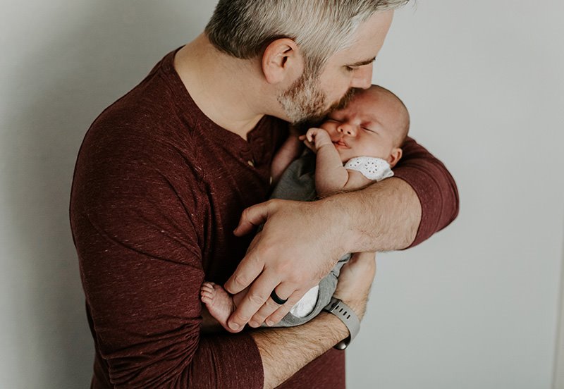 Father holding his baby while giving them a kiss on the forehead, representing good pediatric health