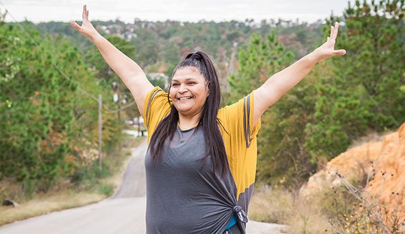 A smiling ARC patient stretching her arms wide during a walk along an Austin road, representing wellness and an active lifestyle