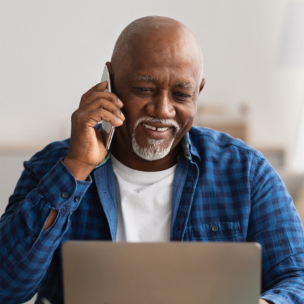 Older man renewing his Medicare insurance plan online while on the phone with a Medicare insurance specialist
