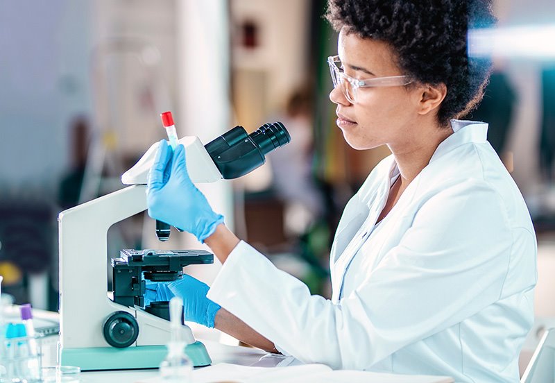 Clinical research specialist examining a vial in front of a microscope