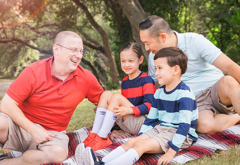 Two fathers and their children having a picnic outside, representing good skin care during the summer time
