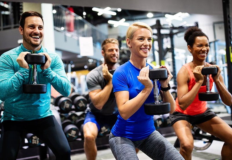 Group of adults squatting using dumbbells at the gym, highlighting fitness and benefits of a DEXA body composition analysis