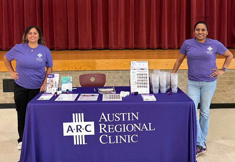 Swapna Manthena, MD, and an ARC team member next to an ARC booth at a health fair hosted by the Health Occupations Students of America (HOSA) chapter at Round Rock High School