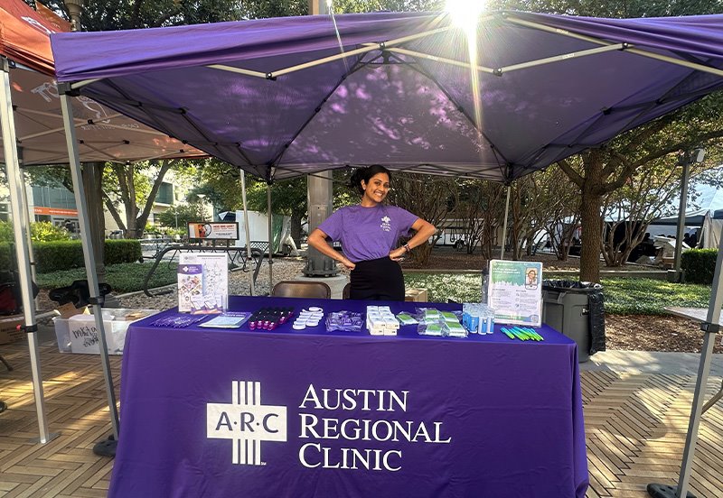 ARC team member standing at the Austin Regional Clinic booth during the 2025 fall UT Marketplace