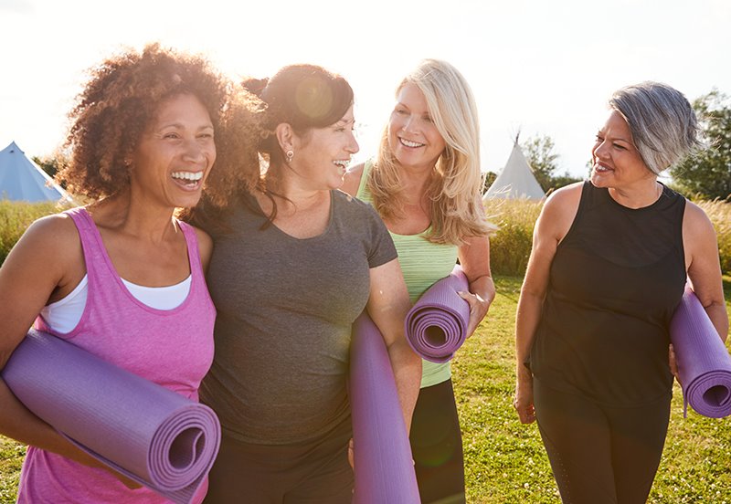 Four women enjoying a good conversation while they each hold a floor mat and prepare for some outdoor exercise, representing an active lifestyle and preventive care