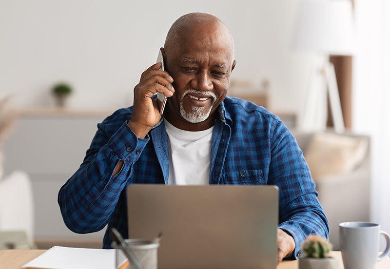 Older man renewing his Medicare insurance plan online while on the phone with a Medicare insurance specialist