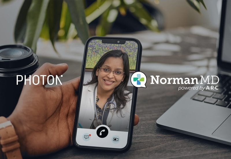 Photon and NormanMD logos with a first-person view of a patient connecting with their NormanMD physician during a virtual visit through their smartphone as the background