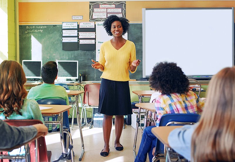 Teacher giving a lesson in a classroom full of students, representing good health following an annual checkup
