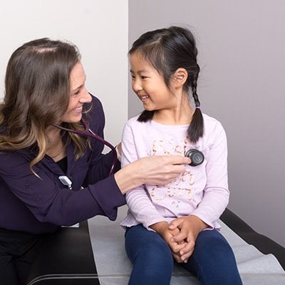 photo of doctor holding stethoscope to young patient